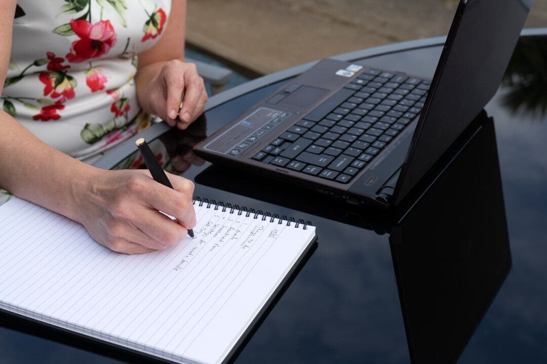 Woman taking notes beside a laptop while reviewing Pinterest metrics